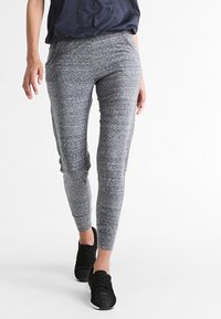 Sportovní legíny v melírované šedé tkanině. Úzký střih se hladkým povrchem, s vysokým pasem a manžetami na kotnících. V kombinaci s černými teniskami.