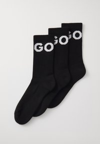 Chaussettes en coton noires, avec un design côtelé, arborant le mot "GO" en lettres blanches sur le haut. Trois paires empilées ensemble.