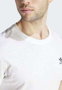 Bílý bavlněný tričko s kulatým výstřihem, na levé hrudi s černým logem Adidas. Měkká textura a přiléhavý střih.