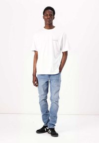 Hvid bomulds t-shirt med et lille trykt logo, parret med lyseblå denim jeans og sorte sneakers med hvide striber.