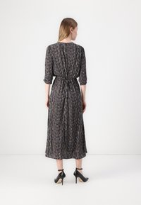 Langes schwarzes Kleid mit strukturiertem Muster, gesammeltem Rücken, Dreiviertelärmeln und einem Bindedetail in der Taille. Getragen mit schwarzen High Heels.