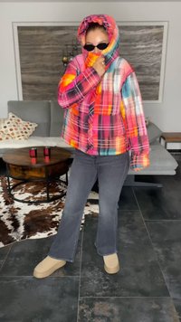 Colorful plaid puffer jacket with a hood, shades, and gray flared jeans. Beige platform shoes complement the outfit. Soft, warm materials visible.