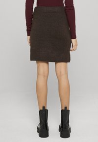 Jupe brune en tricot avec une ceinture côtelée, coupe droite, longueur mi-cuisse, associée à des bottines noires à semelle épaisse.