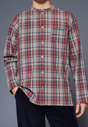 Persona que lleva una camisa a cuadros roja, verde y morada de manga larga y con botones, con un bolsillo en el pecho, y pantalones oscuros de pana.