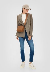 Brązowa marynarka w kratę, kremowy golf, niebieskie dżinsy, beżowa czapka i brązowa torebka na ramię. Buty w kolorze kremowym z platformą.