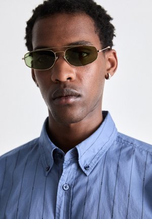 Grüne ovale Sonnenbrillen mit dünnen Metallrahmen, kombiniert mit einem hellblauen Hemd mit Knöpfen, das vertikale Streifen und einen klassischen Kragen aufweist.