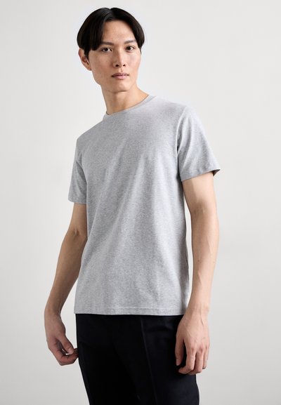 T-shirt gris à manches courtes en coton doux, doté d'un col rond et d'une coupe décontractée. Porté avec un pantalon noir.