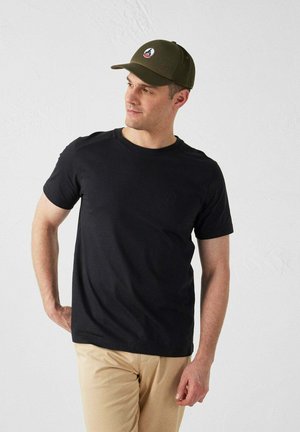 Camiseta negra de manga corta con cuello redondo y un sutil detalle de logo. Combinada con una gorra verde que presenta un logo de parche redondo.