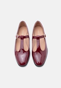 Μαρι Τζέιν παπούτσια από δέρμα βερνίκι σε μπορντό χρώμα με στρογγυλεμένη μύτη, πλευρές με κοψίματα και μικρή μεταλλική αγκράφα στο λουράκι. Φλατ σόλα.