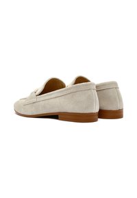 Mocassini beige in suede con un tacco in gomma marrone chiaro basso, caratterizzati da una finitura liscia e dettagli di cucitura sottili.