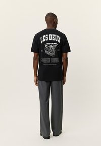 Μαύρο βαμβακερό t-shirt με μεγάλο λευκό κείμενο "LES DEUX" και εικονογραφημένο καλάθι μπάσκετ στην πλάτη· χαλαρή εφαρμογή, σχεδίαση με στρογγυλή λαιμόκοψη.