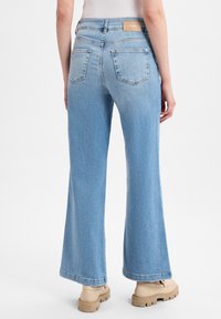 Ljusblå, högmidjade utsvängda jeans med en slät textur, bakfickor, kontrasterande sömmar och en logolapp på midjebandet.