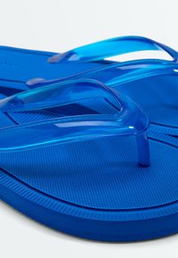 Paire de tongs bleues avec semelles texturées et brides en plastique translucide sur fond blanc.