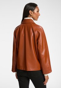 Giubbotto in pelle marrone con una vestibilità rilassata, grande colletto e spalle basse. Presenta una texture liscia e dettagli di cucitura puliti.
