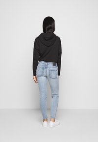 Sudadera corta negra con capucha, combinada con vaqueros ajustados de color azul claro y zapatillas blancas, que muestran un ajuste relajado y un aspecto casual.