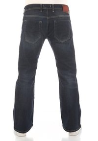 Jean en denim bleu foncé avec une coupe droite, cinq poches et des coutures visibles. Patch en cuir à la taille.