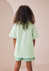 Tricou supradimensionat verde mentă cu mâneci scurte, asortat cu pantaloni scurți verzi cu dungi. Textură netedă de bumbac, design simplu și croială lejeră.