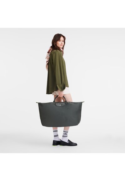 Grey nylon tote bag with two top handles, featuring a logo patch and zip closure. Paired with a green top and beige shorts.