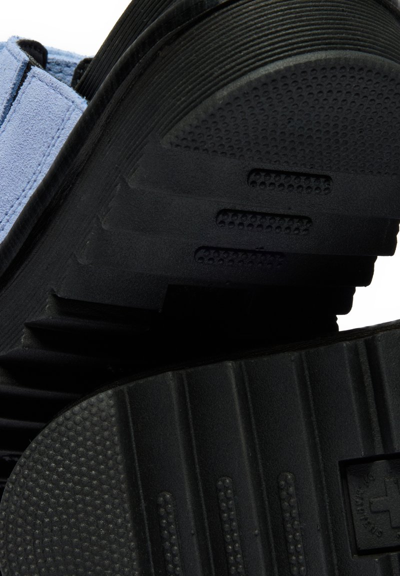Close-up of black soles showing textured tread patterns and part of light blue fabric upper on footwear.