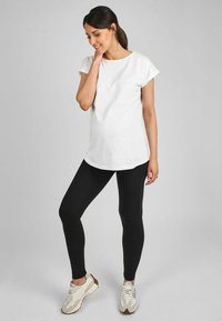 Biely krátky rukáv s prehodenými manžetami, nosený s čiernymi legínami a svetlými teniskami. Neformálny outfit s voľným strihom.