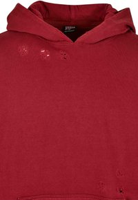 Felpa rossa con cappuccio realizzata in miscele di cotone con una finitura testurizzata, caratterizzata da dettagli consumati e una grande tasca frontale a marsupio.