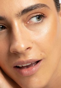 Nærbilde av et ansikt med glatt, solbrun hud. Kjennetegn inkluderer fyldige lepper, definerte øyenbryn og klare grønne øyne med en lett reflekterende tekstur.