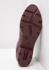 Semelle de chaussure en caoutchouc bordeaux avec une surface texturée, motif de traction moulé, marquage de taille 37 et détail en découpe circulaire.