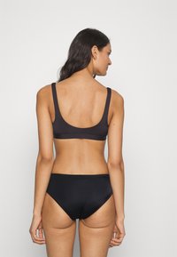Juodas bikini rinkinys su paprastu dizainu, plačiomis petnešomis ir žemu nugaros pjūviu. Lygi, tampri medžiaga su vidutiniu padengimu apatinėje dalyje.