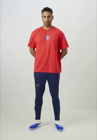 Camiseta roja de Nike con un logo azul de París, combinada con pantalones azul marino que presentan el texto dorado "PARÍS", y zapatillas de fútbol azules con acentos blancos.