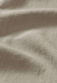 Tessuto in lino beige chiaro con una superficie texturizzata, che mostra morbide pieghe e una leggera lucentezza, enfatizzando la sua qualità naturale e traspirante.