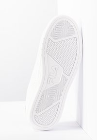 Suola di sneaker in gomma bianca con motivo di grip testurizzato e logo in rilievo. Presenta bordi arrotondati e fori di ventilazione laterali.