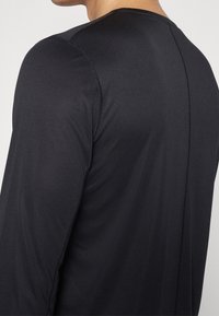 Pitkähihaista mustaa paitaa, joka on valmistettu sileästä ja kevyestä materiaalista. Sisältä ä tasaisia saumoja ja yksinkertaisen, virtaviivaisen muotoilun.