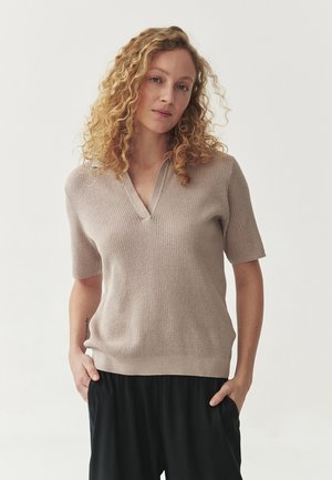 Korte mouwen, v-hals trui in lichtbeige, met een gestructureerd breipatroon en ribgebreide zoom. Draag het met losse zwarte broek.