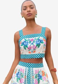 Virágmintás crop top és szoknya szett, fehér anyagból, kék és rózsaszín virágmintákkal; négyzet alakú dekoltázzsal és geometrikus díszítéssel rendelkezik.