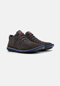 Zwarte sportieve schoenen met een bovenwerk van gaas en suède accenten. Voorzien van grijze veters en een blauwe rubberen zool. Achterop een logo-tag in het rood.