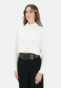 Maglione bianco corto con collo alto alla coreana, orlo a costine e maglia lavorata a trama. Abbinato a pantaloni neri a vita alta con cintura doppia fibbia.