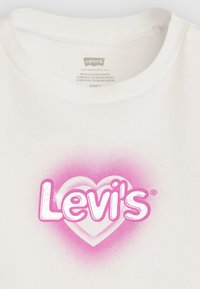 Bílý bavlněný tričko s velkým růžovým srdcem a slovem "Levi's" tučně napsaným bílým textem, měkká textura a kulatý výstřih.