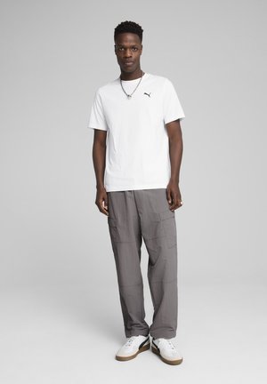 Hvid t-shirt med korte ærmer og sort logo, parret med grå cargo-bukser med sidelommer og struktureret stof, suppleret med hvide sneakers.