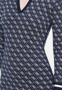 Maglione in maglia blu navy con scollo a V e motivo geometrico bianco su tutta la superficie. Presenta maniche lunghe e polsini e orlo a costine.