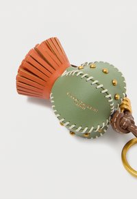 Nahkane võtmehoidja rohelise, õmmeldud kehaga, kuldsete nukkide ja oranži fännilaadse ülaharjaga. Sisaldab kuldset võtmehoidjat.