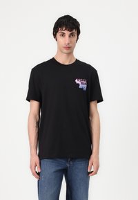Sort bomulds T-shirt med korte ærmer, der har et farverigt gradient-logo på venstre bryst. Designet er enkelt og afslappet.