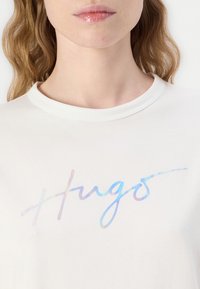 Tricou alb cu un logo holografic "Hugo". Materialul este moale, cu un design clasic la gât.