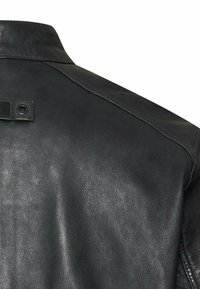 Czarna skórzana tylna część kurtki z przeszywanym kołnierzem i małą skórzaną klapą z metalowym oczkiem przy ramieniu.