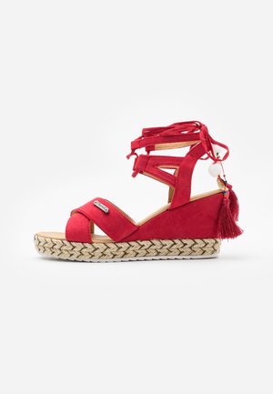 Rode suède wedge sandaal met omslingerende banden, open teen en decoratieve franje. Voorzien van een geweven jute zool voor extra textuur.
