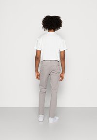 Chinos gris clair avec une coupe slim, dotés de poches arrière avec fermetures à boutons et d'un t-shirt blanc. Portés avec des baskets blanches.