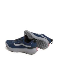 Une paire de baskets de trail Vans bleu marine et gris avec des semelles robustes, des lacets noirs et des tirants sur un fond blanc.