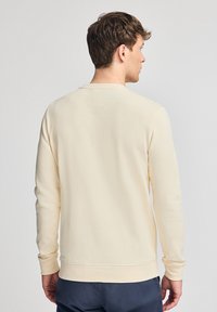 Sudadera de color crema hecha de tela suave, con cuello redondo, mangas largas y puños elásticos, con un diseño sencillo y sin patrones.