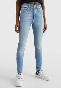 Jeans de tiro alto en un azul claro, ajustados y con una textura desgastada, que cuentan con cinco bolsillos. Combinados con zapatillas blancas que tienen acentos multicolores.