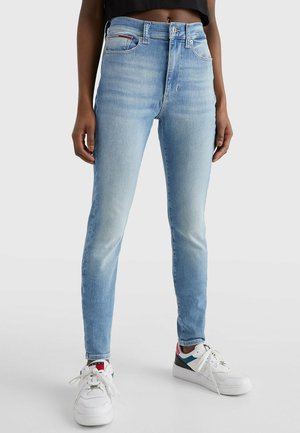 Jeans de tiro alto en un azul claro, ajustados y con una textura desgastada, que cuentan con cinco bolsillos. Combinados con zapatillas blancas que tienen acentos multicolores.