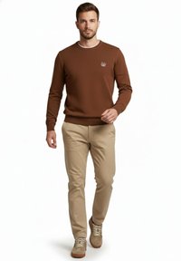 Suéter marrón texturizado con cuello redondo, pantalones chinos beige y zapatillas de ante marrón. Presenta un pequeño logo bordado en el pecho.